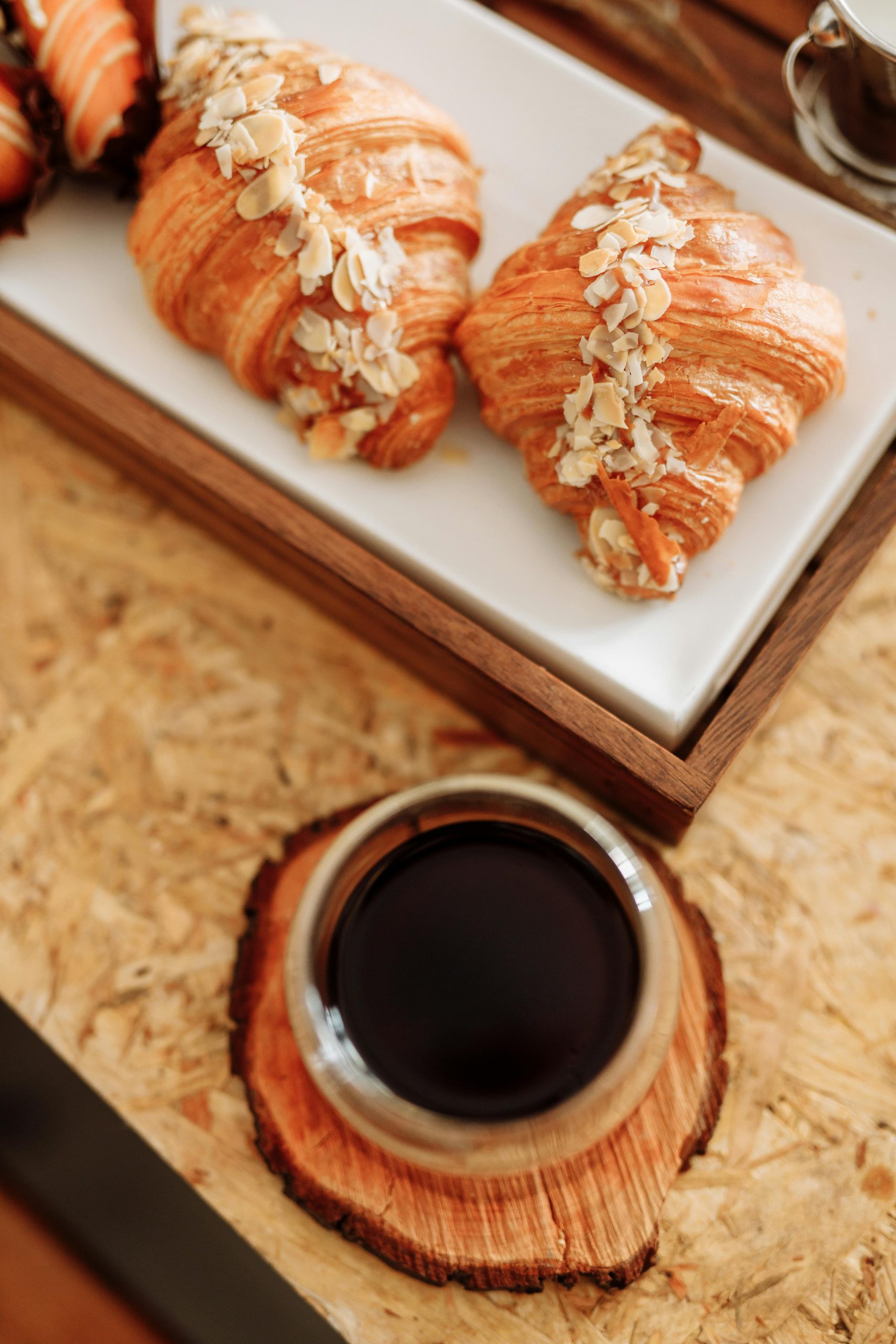 Fresh almond croissants served with coffee on a rustic wooden table.